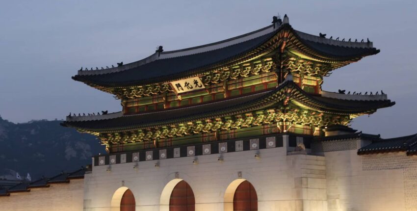 Porte illuminée du palais de Gyeongbokgung avec des piétons au crépuscule.