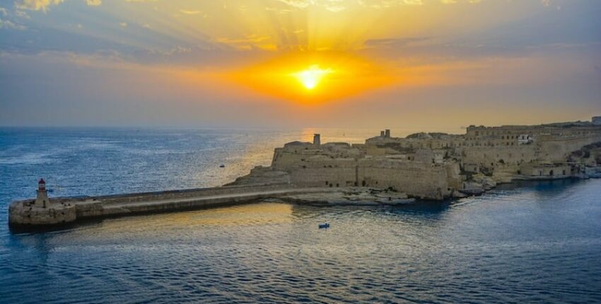 Coucher de soleil sur forteresse côtière et phare.