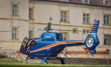 Hélicoptère bleu à rayures orange devant bâtiment.