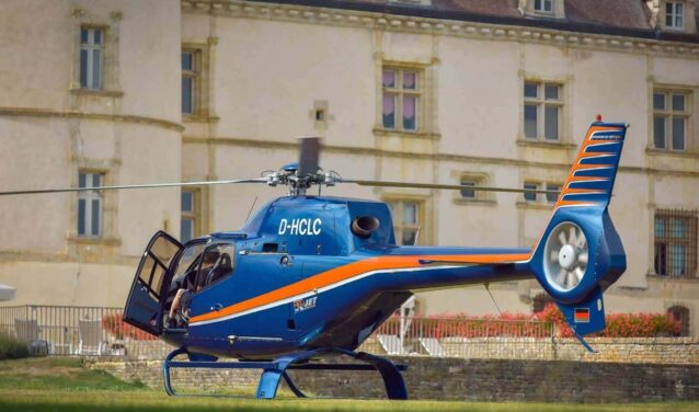Hélicoptère bleu à rayures orange devant bâtiment.