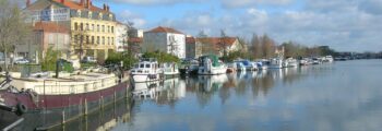 Vue panoramique Roanne, rivière calme, bateaux à quai, journée ensoleillée.